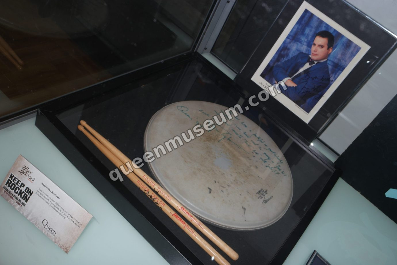 Close view of Roger Taylor’s snare drum head and exhibition card, with a signed Freddie Mercury photo from The Miracle period behind