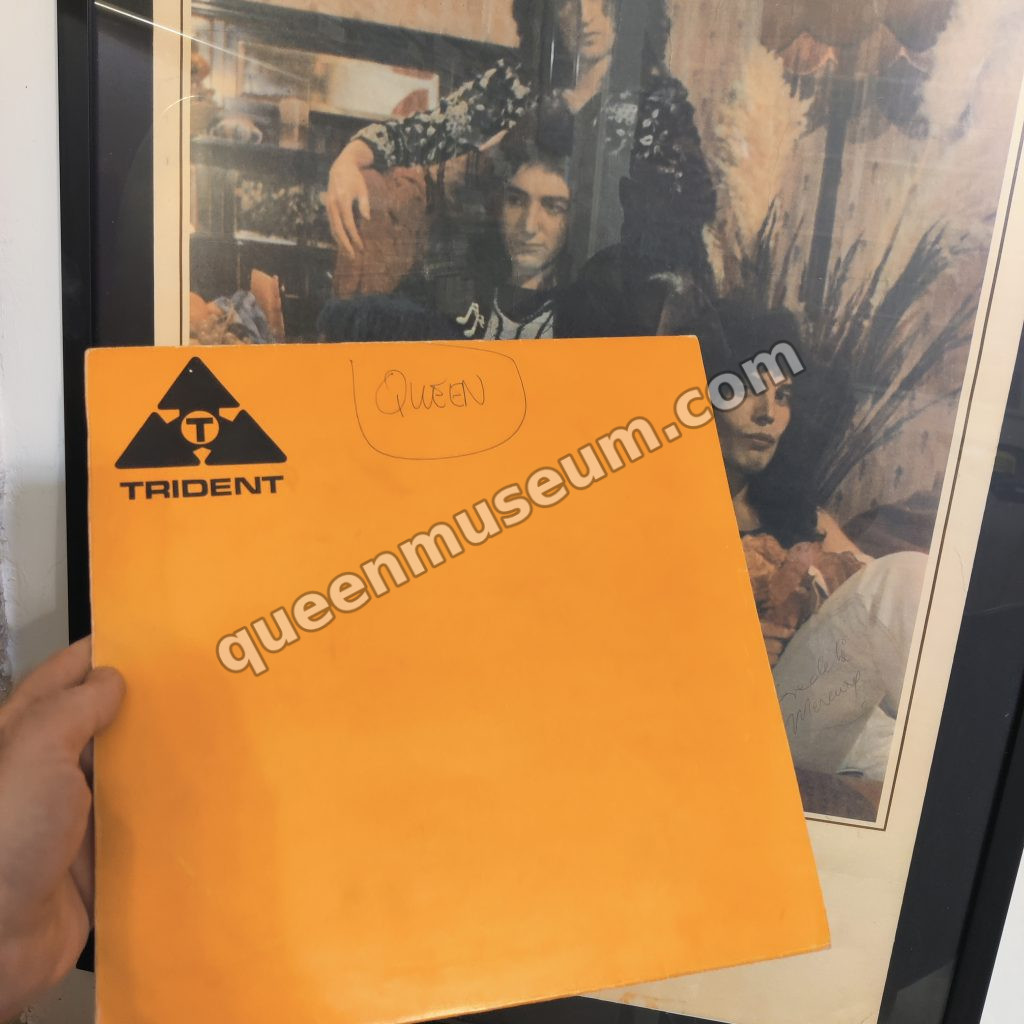 Trident-sleeve acetate of the debut album, containing a different version of Keep Yourself Alive, held up against the UK promotional poster for the album